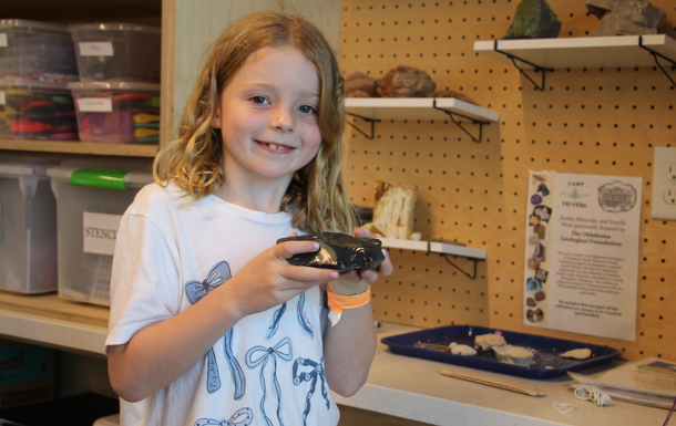 A young girl holds a black rock in the Camp Trivera STEM lab